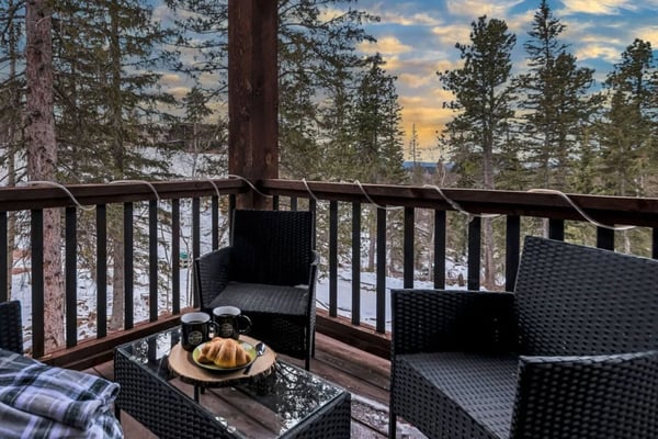 Modern log cabin with wraparound deck, hot tub, and blue seating on lower patio surrounded by pine trees